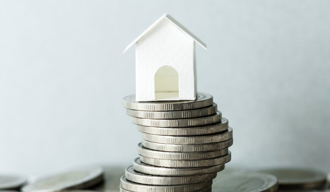 Imagem mostra miniatura de casa em cima de moedas